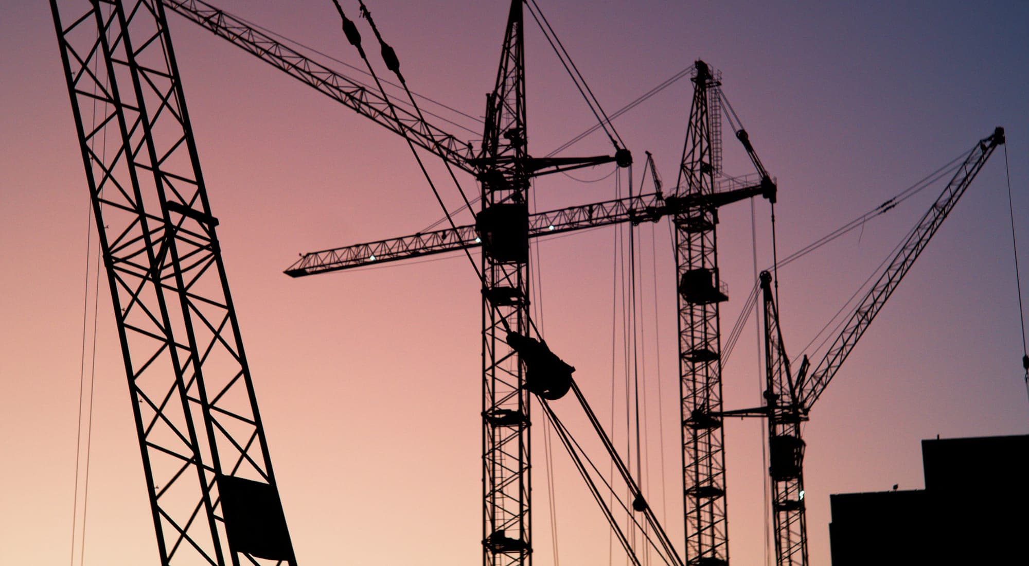 Tower cranes silhouetted against a dusk sky over a construction site